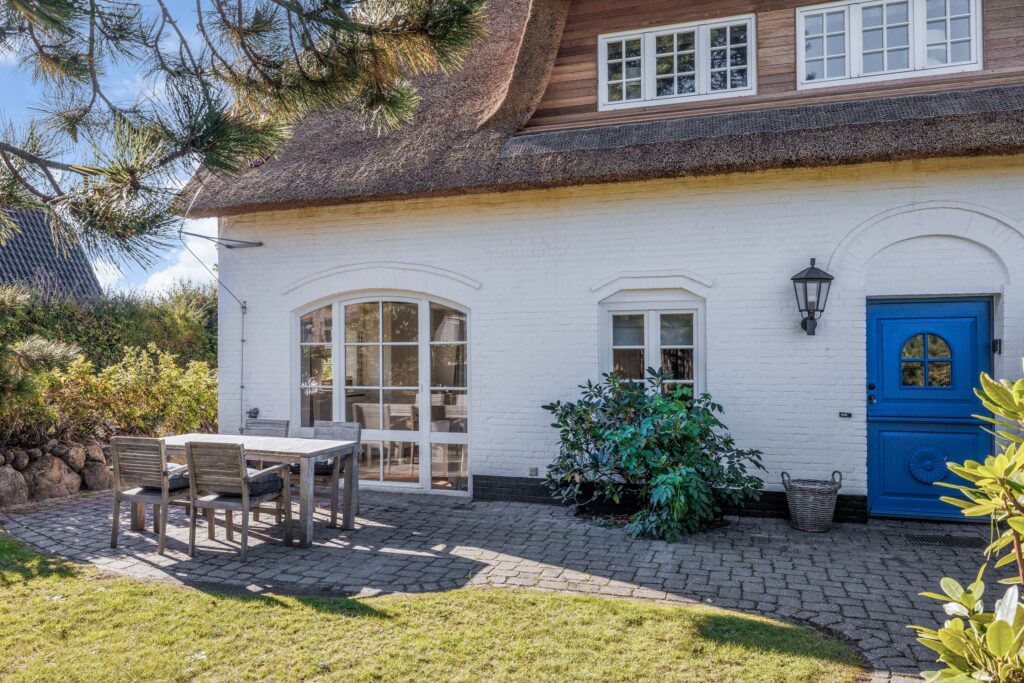 Uriges Reetdachhaus auf Sylt mit weißer Wand und blauer Tür